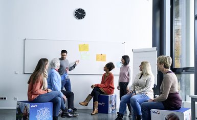 Teilnehmende sitzen in einem Volkshochschulkurs mit einem Dozenten